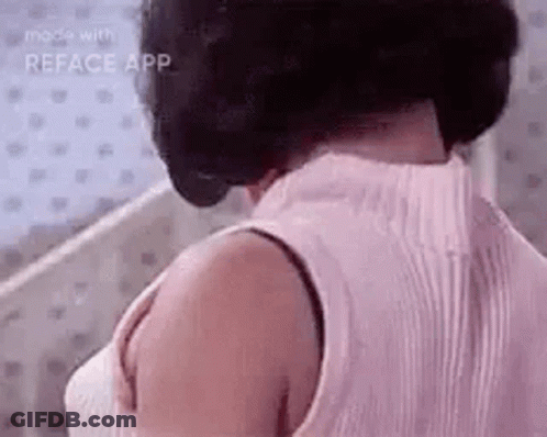 A Woman Wearing A Pink Tank Top And A Bra Is Standing In Front Of A Mirror . GIF
