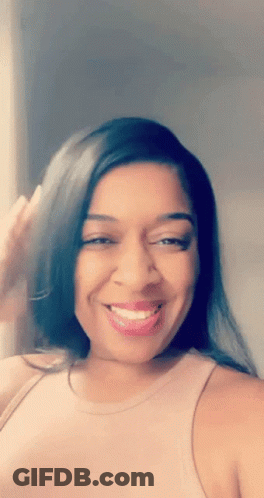 A Woman Wearing A Pink Tank Top Is Smiling And Looking At The Camera GIF