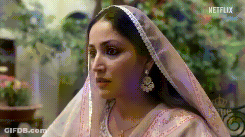 A Woman Wearing A Pink Veil And Earrings Is Looking At Something . GIF