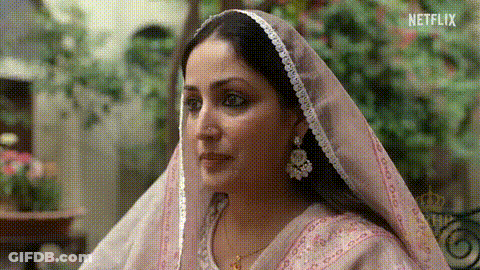 A Woman Wearing A Pink Veil And Earrings Is Looking At Something . GIF