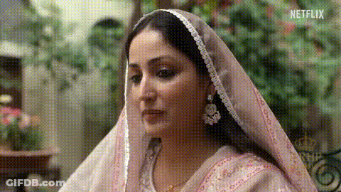 A Woman Wearing A Pink Veil And Earrings Is Looking At Something . GIF