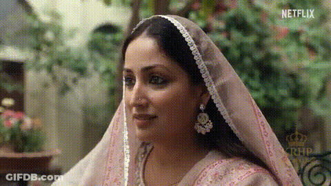 A Woman Wearing A Pink Veil And Earrings Is Looking At The Camera . GIF