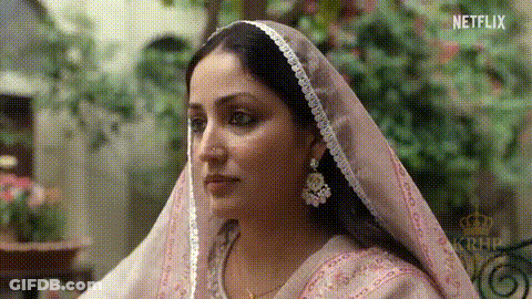 A Woman Wearing A Pink Veil And Earrings Is Sitting Down . GIF