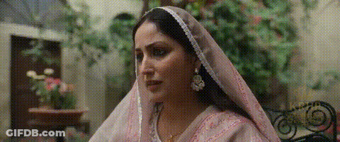 A Woman Wearing A Pink Veil And Earrings Is Sitting On A Chair . GIF