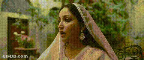 A Woman Wearing A Pink Veil And Earrings Is Standing In A Room . GIF