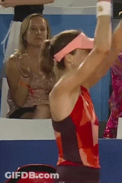 A Woman Wearing A Pink Visor And A Red Top Is Serving A Tennis Ball GIF