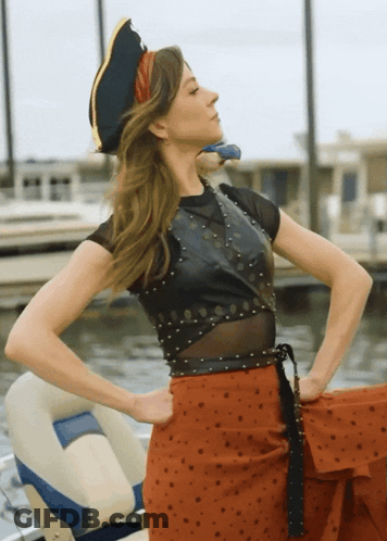 A Woman Wearing A Pirate Hat Is Standing In Front Of A Body Of Water GIF