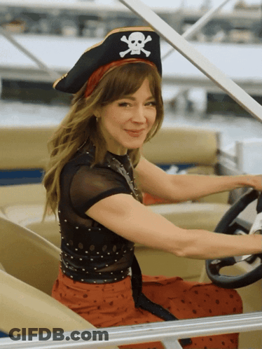 A Woman Wearing A Pirate Hat With A Skull And Crossbones On It Is Driving A Boat GIF