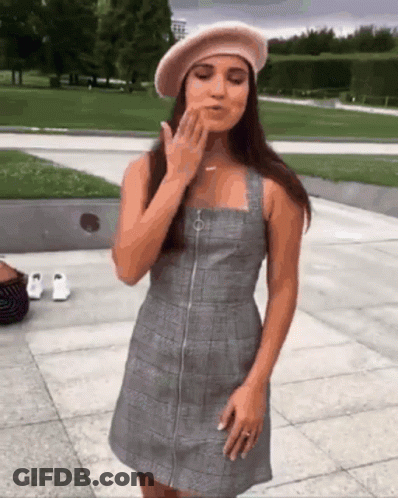 A Woman Wearing A Plaid Dress And A Beret Blows A Kiss GIF