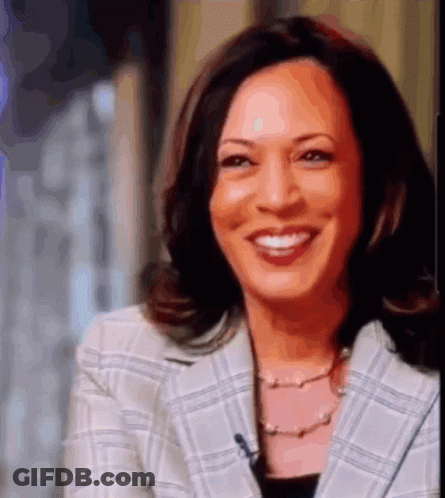 A Woman Wearing A Plaid Jacket And A Pearl Necklace Is Smiling GIF