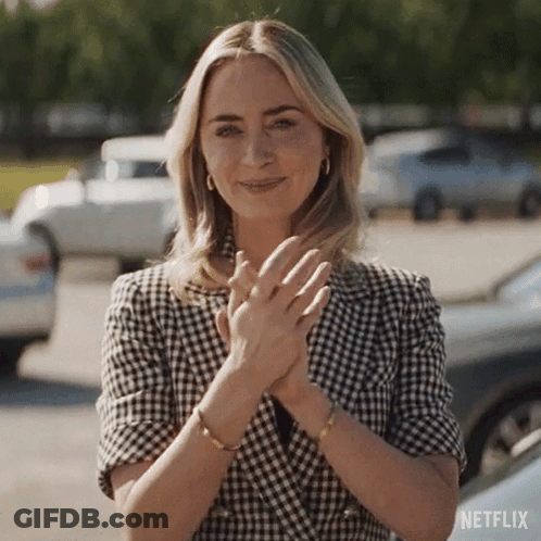 A Woman Wearing A Plaid Jacket Is Clapping Her Hands In A Parking Lot . GIF