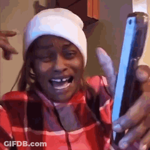 A Woman Wearing A Plaid Shirt And A Beanie Is Holding A Cell Phone . GIF