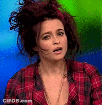 A Woman Wearing A Plaid Shirt And A Necklace Is Making A Funny Face GIF