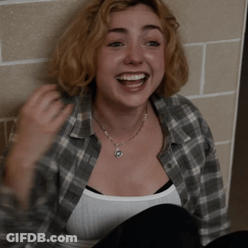 A Woman Wearing A Plaid Shirt And A White Tank Top Smiles GIF