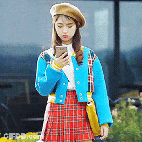 A Woman Wearing A Plaid Skirt And A Beret Looks At Her Phone GIF