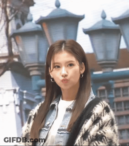 A Woman Wearing A Plaid Sweater And A Denim Jacket Is Standing In Front Of Street Lights GIF