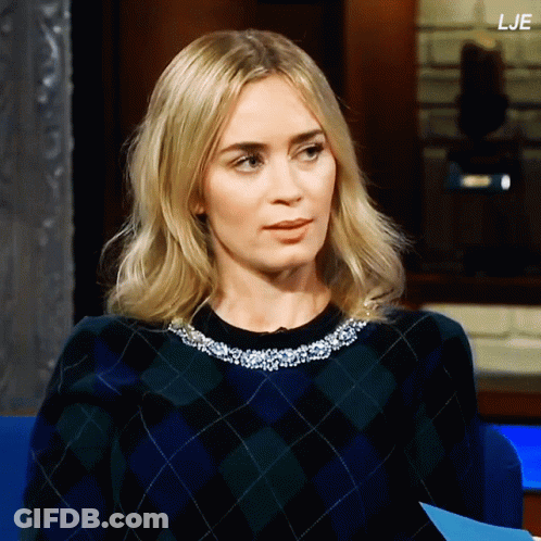 A Woman Wearing A Plaid Sweater Is Sitting In Front Of A Sign That Says " Lje " GIF