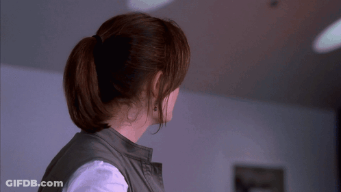 A Woman Wearing A Ponytail And Earrings Looks To The Side GIF