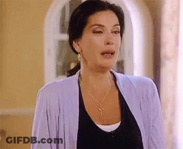 A Woman Wearing A Purple Cardigan And A Black Shirt Is Standing In A Room . GIF