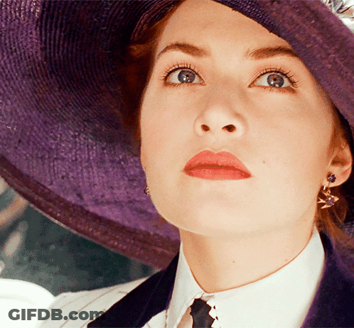A Woman Wearing A Purple Hat And Earrings Looks Up At Something GIF