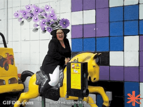 A Woman Wearing A Purple Hat Is Riding A Yellow Horse That Says And The Winner Is GIF