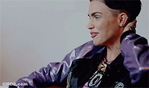 A Woman Wearing A Purple Jacket And A Black Hat Is Sitting In A Chair GIF