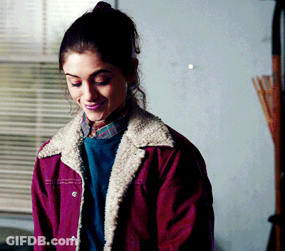 A Woman Wearing A Purple Jacket And A Plaid Shirt Smiles GIF