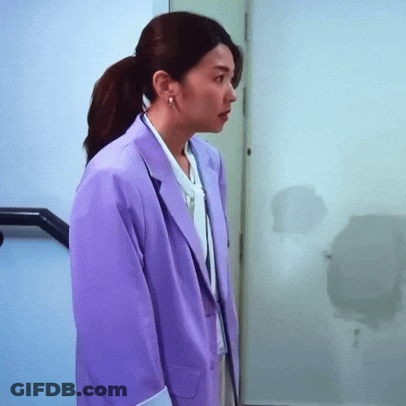 A Woman Wearing A Purple Jacket And A White Shirt Is Standing In A Hallway . GIF
