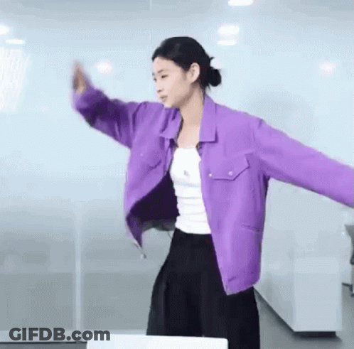 A Woman Wearing A Purple Jacket And A White Tank Top Is Dancing In A Room . GIF
