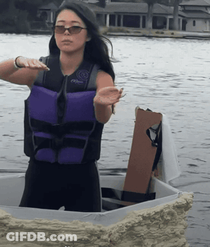 A Woman Wearing A Purple Life Vest And Sunglasses Stands In The Water GIF