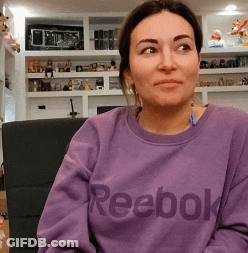 A Woman Wearing A Purple Reebok Sweatshirt Looks At The Camera GIF