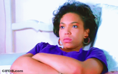 A Woman Wearing A Purple Shirt And Hoop Earrings Is Laying On A Bed With Her Arms Crossed GIF