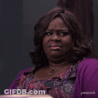 A Woman Wearing A Purple Sweater And A Floral Dress Is Making A Face . GIF