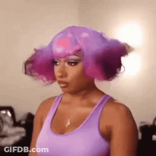 A Woman Wearing A Purple Tank Top And A Purple Wig Is Standing In A Room . GIF