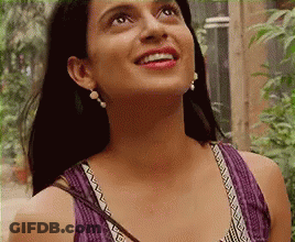 A Woman Wearing A Purple Tank Top And Earrings Is Smiling While Looking Up . GIF