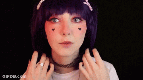 A Woman Wearing A Purple Wig And A Choker Is Smiling And Making A Peace Sign . GIF