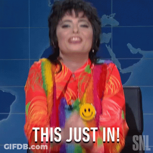 A Woman Wearing A Rainbow Shirt And A Smiley Face Necklace Says This Just In GIF