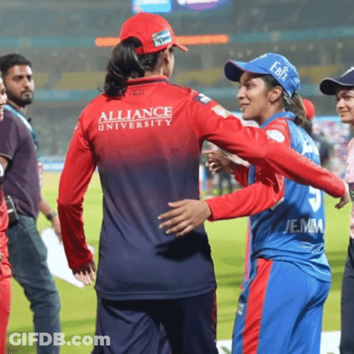 A Woman Wearing A Red Alliance University Jersey Is Hugging Another Woman GIF