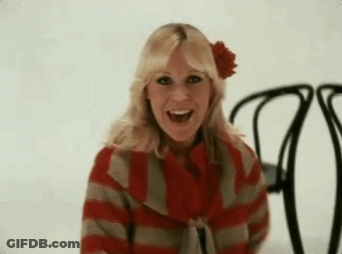 A Woman Wearing A Red And Gray Striped Sweater And A Red Flower In Her Hair Is Sitting In A Chair . GIF