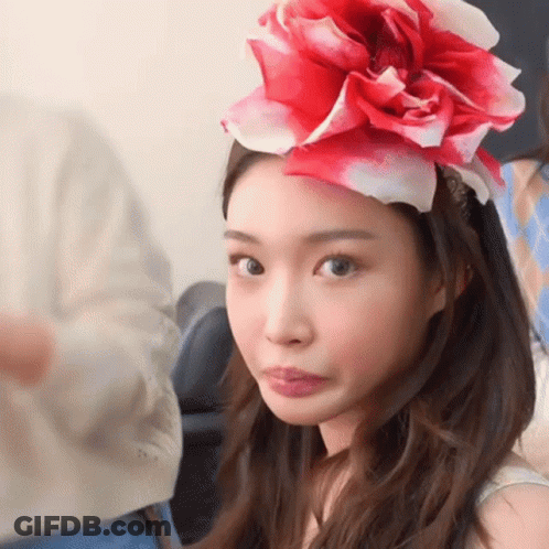 A Woman Wearing A Red And White Flower On Her Head Making A Face GIF