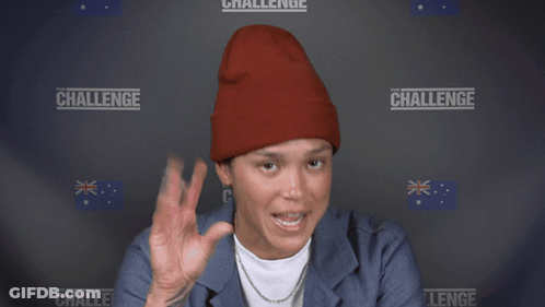 A Woman Wearing A Red Beanie Is Smiling In Front Of A Wall With The Word Challenge On It GIF