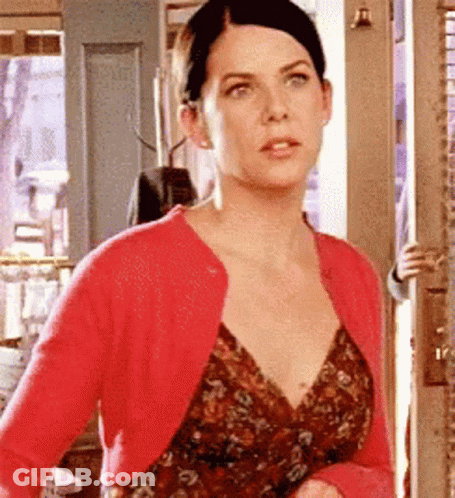 A Woman Wearing A Red Cardigan And A Floral Dress Is Standing In A Doorway . GIF
