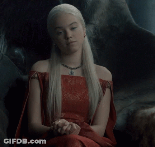 A Woman Wearing A Red Dress And A Necklace Sits In A Chair GIF