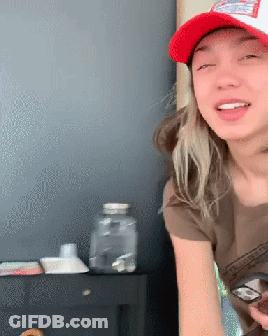 A Woman Wearing A Red Hat And A Brown Shirt Is Holding A Cell Phone . GIF