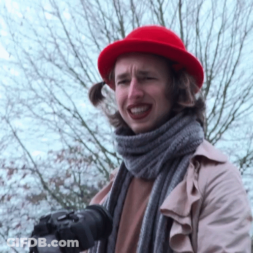 A Woman Wearing A Red Hat And A Scarf Holds A Camera GIF