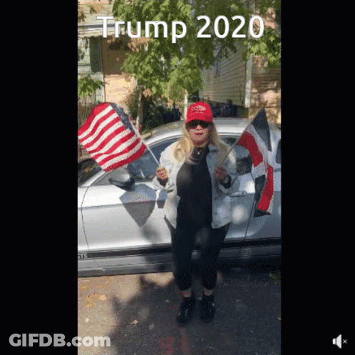 A Woman Wearing A Red Hat That Says Trump 2020 Stands In Front Of A Silver Car GIF