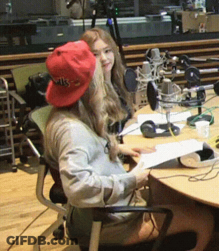 A Woman Wearing A Red Hat That Says Wks Sits At A Desk GIF