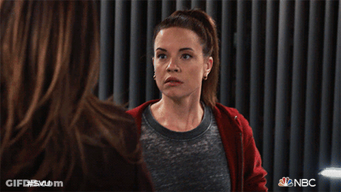 A Woman Wearing A Red Hoodie Is Sitting In Front Of A Curtain With Nbc Written On It GIF