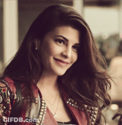 A Woman Wearing A Red Jacket And A Necklace Is Smiling For The Camera GIF