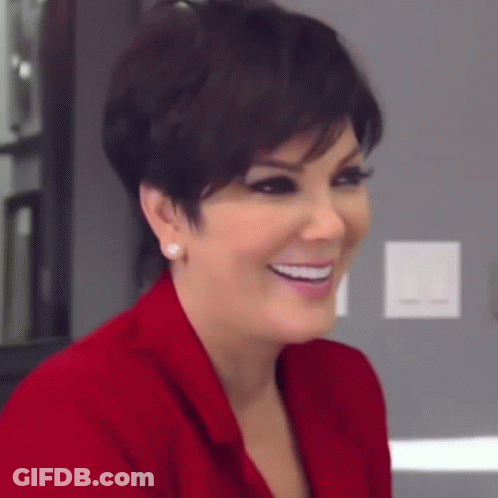 A Woman Wearing A Red Jacket And Earrings Is Smiling And Looking At The Camera . GIF